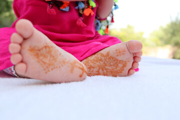 Shallow focus of charming small feet with traditional Moroccan henna tattoo on a white blanket