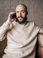 young bald man with a beard is talking on the phone in the room