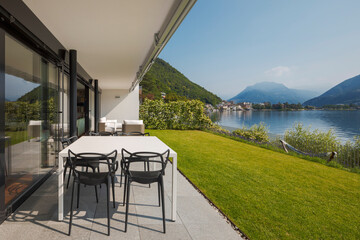 Modern house of two apartments with a beautiful garden directly on Lake Ceresio. Sunny day with blue sky. Minimalist and linear architecture. Panoramic view of the lake. Space for your text