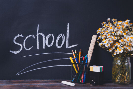 inscription school on a blackboard, pens, pencils , chalk, chamomile flowers