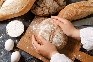 hands hold a round loaf of bread on a board on the table, rye and wheat bread, flour ,eggs,