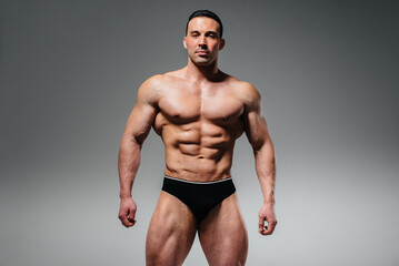 A young athlete bodybuilder poses in the studio topless, showing off his abs and muscles. Sport.