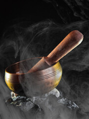 Tibetan bowl with stick on stones with black background and softly lit with smoke in the image