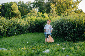A seven-year-old boy at sunset is engaged in garbage collection in the park. Environmental care,...
