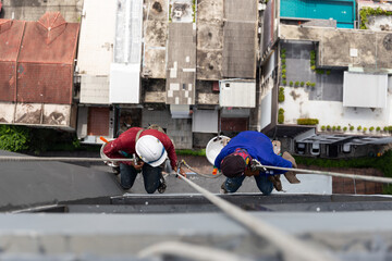 Asian painters hanging on rope painting color on building wall.