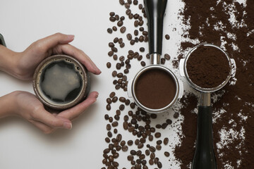 Hand holding a cup of coffee and portafilers with coffee beans