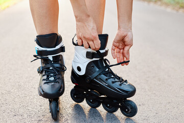 Close-up of an anonymous woman hands fixing laces on roller blades during skating, unknown female...