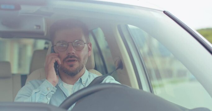 Young bearded tourist man driving around the city and searching for suitable direction while looking at at the road and calling by the smartphone. People at the wheel concept