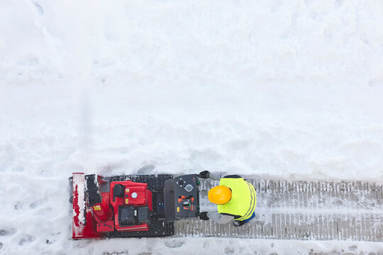 Worker cleaning snow on the sidewalk with a snowblower. Wintertime