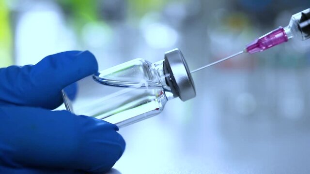 Close-up of doctor or scientist hand holds a syringe and a transparent vaccine bottle at the hospital. Medical care concept