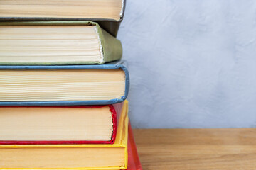 Stack of colorful hardback books on wooden table close up against gray and blue concrete wall