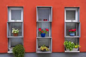 Fototapeta na wymiar View of a red house facade with three windows decorated with flowers 