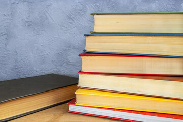 Stack of multi-colored hardback books on wooden table against gray-blue concrete wall