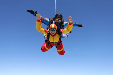 Skydiving. Tandem jump. A happy passenger and her instructor are flying in the sky. - obrazy, fototapety, plakaty