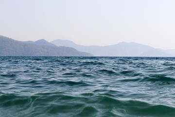 Scenic view from sea water surface to misty mountains covered with forest. Beach vacation, background for summer travel