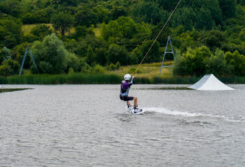 Woman practicing wakeboarding on a lake with green hills in cloudy day