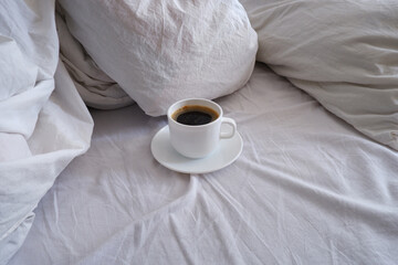 A cup of black coffee in a white bed. Breakfast in bed. Interior.