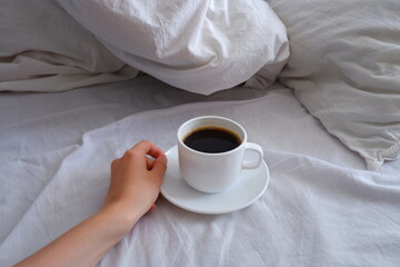 The girl is drinking coffee in bed. A cup of black coffee in a white bed. Breakfast in bed. Interior.
