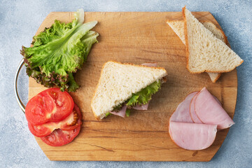 Fototapeta na wymiar Delicious healthy sandwich for a snack breakfast on a wooden cutting board, top view. Toast bread tomato ham leaf salad.