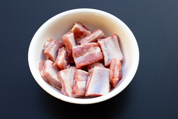 Raw pork ribs in white bowl on dark background.