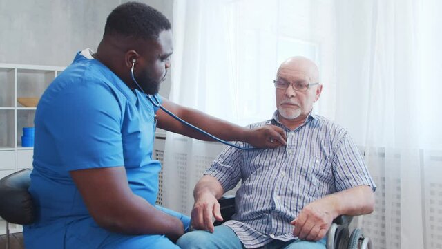 African-American caregiver and old disabled man in a wheelchair. Professional nurse and handicapped patient in a nursing home. Assistance, rehabilitation and health care.