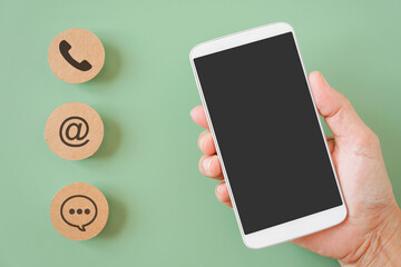 hand holding white mobile phone with clipping path on touchscreen and blurred brown contact method paper, contact us, call, mail or chat, question and answer ,new normal lifestyle , social distancing