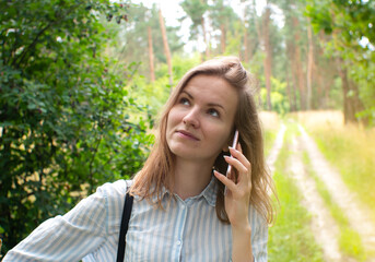 Beautiful girl with fair hair is talking on phone in forest. Young woman lost on the nature. No signal phone connection.