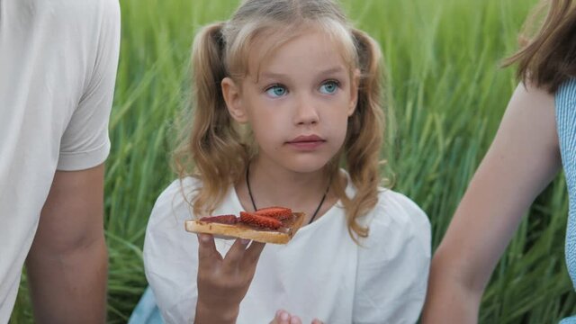 Cute little girl eating chewing chocolate sandwich with strawberry on outdoor picnic