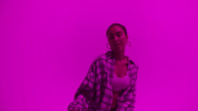 Attractive talented woman dancing hip hop on purple neon background in studio. Shooting of modern choreography for advertising of dance school, dancer expressing feelings for music video performance.