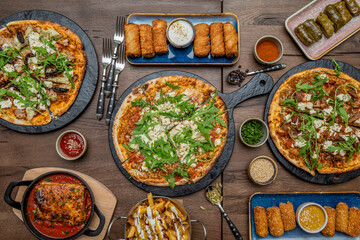 Small pizzas with lots of arugula, lasagna with tomato, sarma on a pink plate, croquettes and rolls. Cardamom, pepper and potatoes with bacon and cheeses