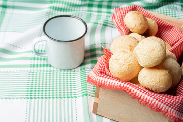 Brazil Cheese Bread, box with cheese buns and a cup on a green checkered tablecloth, selective focus.