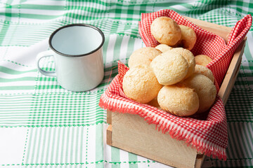 Brazil Cheese Bread, box with cheese buns and a cup on a green checkered tablecloth, selective focus.