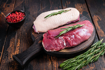 Raw Duck breast  fillet steaks on wooden cutting board with rosemary. Dark wooden background. Top...