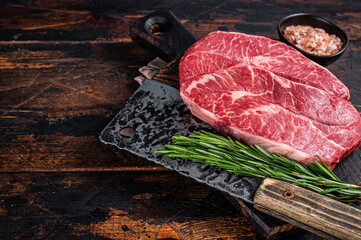 Uncooked Raw Shoulder Top Blade or flat iron beef meat steaks on a wooden butcher board with meat...