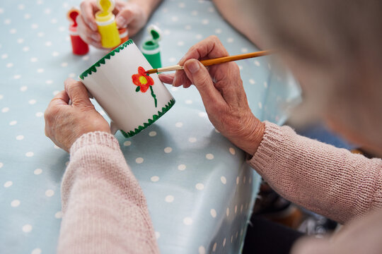 Close Up Of Senior Woman Painting Cup With Art Therapist