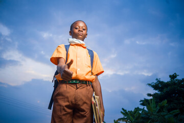 below angle view of african kid holding books and a backpack with a thumb up sign-