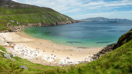 Panorama image of Keem bay beach on a warm sunny day. Achill island, county Mayo, Ireland, Irish landscape. Tourists on the beach, Blue cloudy sky. Beautiful blue ocean color