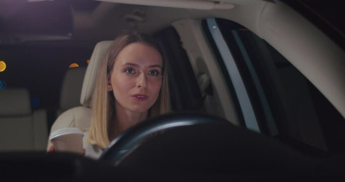 Dont sleep. Happy caucasian woman drinking her hot coffee and looking at the road while driving the car at the dark night. Energetic concept