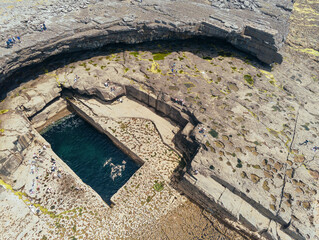 Aerial drone view on famous Poll na bPéist - The Wormhole, Inishmore, Aran islands, county Galway, Ireland. Popular tourist hike and landmark, Warm sunny day. Tourist swimming inside nature pool