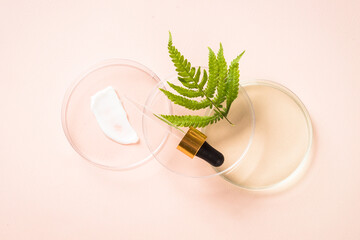 Cosmetic laboratory concept. Glass petri dish with different cosmetic products and green plants. Top view at pastel background.