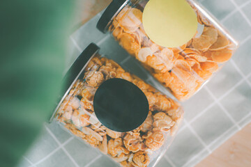 Two cans of popcorn in a clear plastic tin can, capped and labeled, flat lay, top view image