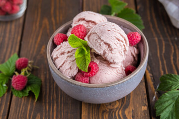 Balls of raspberry ice cream with fresh raspberries in a ceramic bowl on a brown wooden background. Ice cream recipes.