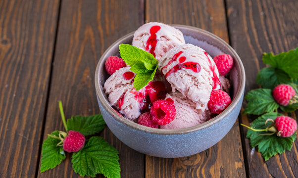 Balls of raspberry ice cream with fresh raspberries in a ceramic bowl on a brown wooden background. Ice cream recipes.