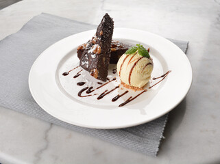 walnut chocolate brownie with vanilla ice cream and peanut, chocolate sauce, mint leaf dessert on round plate western pastry halal menu