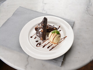walnut chocolate brownie with vanilla ice cream and peanut, chocolate sauce, mint leaf dessert on round plate western pastry halal menu