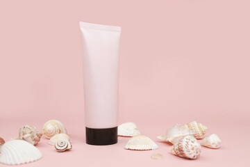 Unbranded pink squeeze bottle plastic tube with black cap and a lot of different sea shells on pink background. Mockup with copy space. Cosmetic bottle for branding and label, front view, closeup.