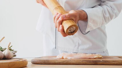 Cropped view of chef with mill seasoning chicken meat on chopping board on white