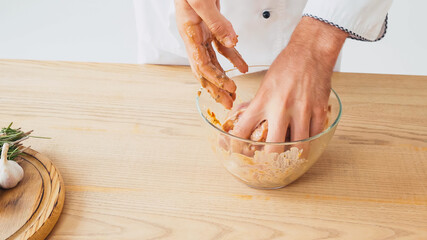 Cropped view of chef marinating sliced chicken in bowl on white background