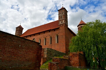 Fototapeta na wymiar A close up on an old medieval castle made out red brick and stone with some towers and an angled roof seen next to the remnants of medieval walls that are partially damaged spotted in summer in Poland