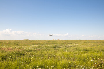 Flying white drone quadcopter with digital camera in green field in the distance